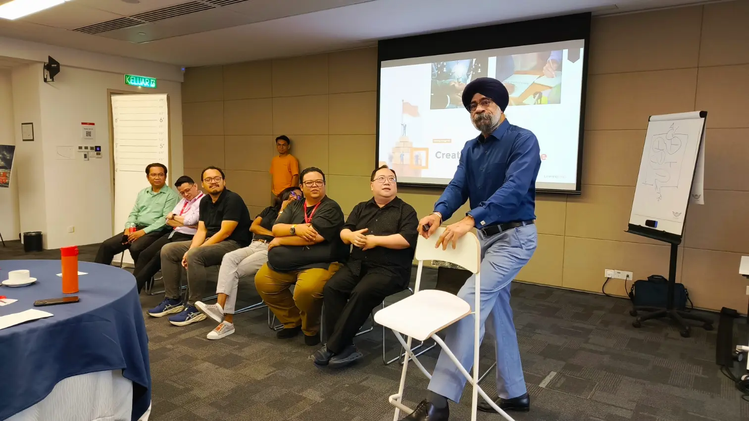 A Learning Edge trainer standing on a chair to address a seated group during a leadership session